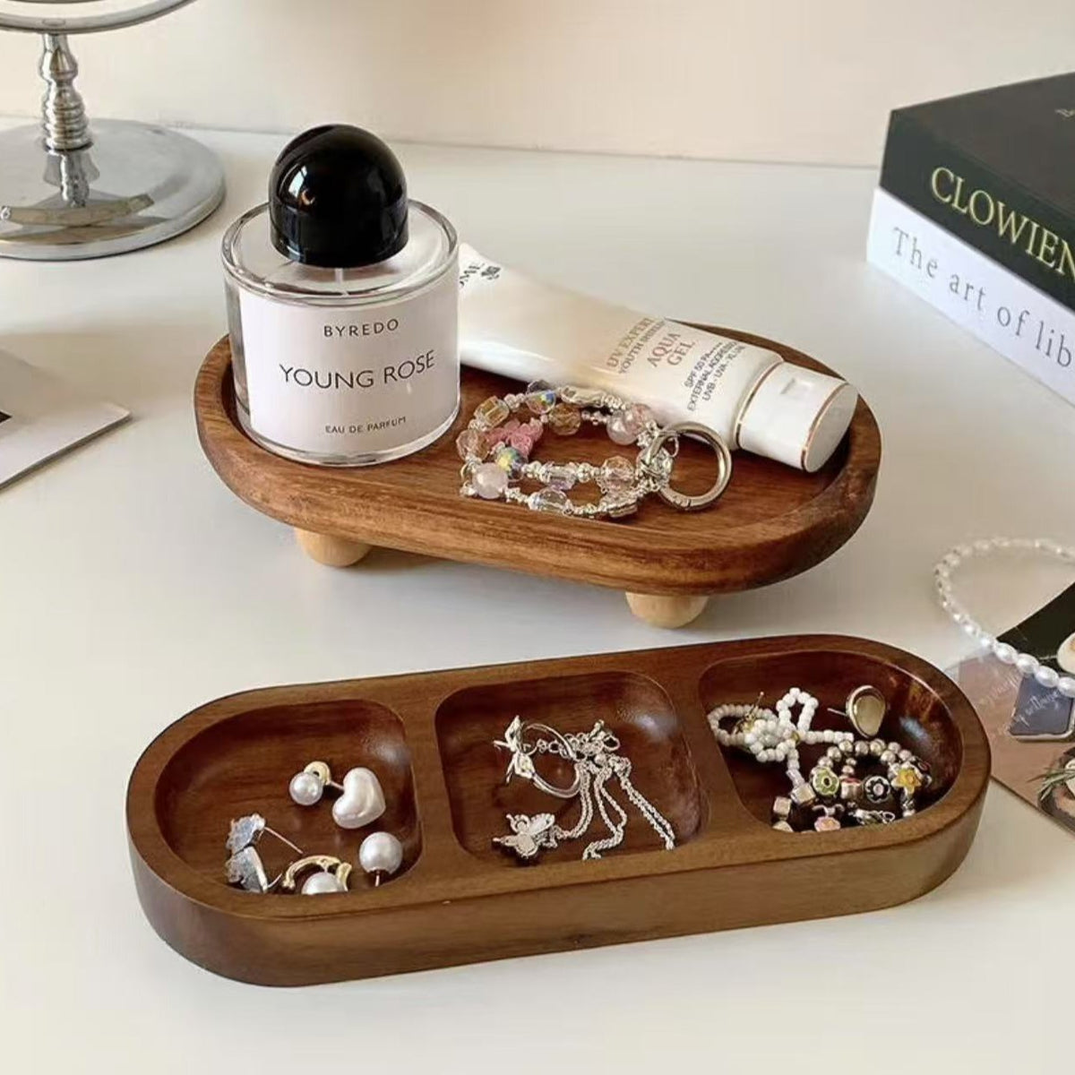 Walnut jewelry trays with earrings and bracelets beside a perfume bottle on a white desk – Pausadesk