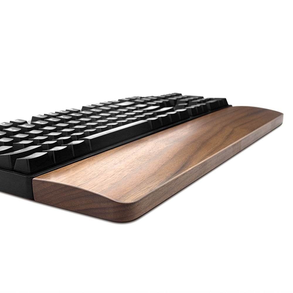 Side angle of the walnut wrist rest showing rounded edges and wood grain beside a keyboard – Pausadesk