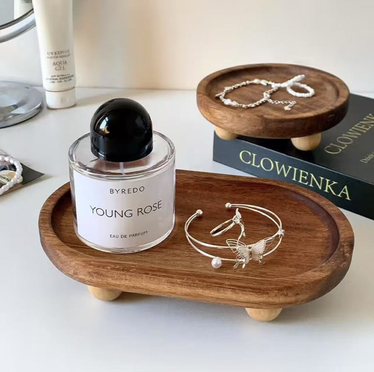 Two walnut oval trays holding a perfume bottle and butterfly bracelet on a vanity desk – Pausadesk