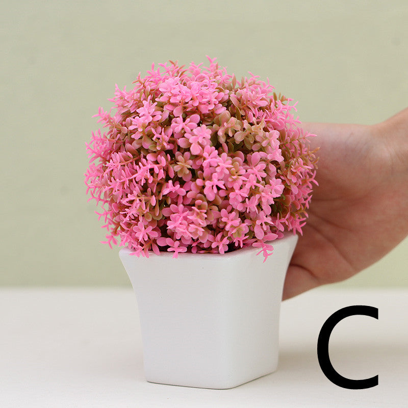Pink artificial mini plant in white square pot, held by hand for scale – Pausadesk