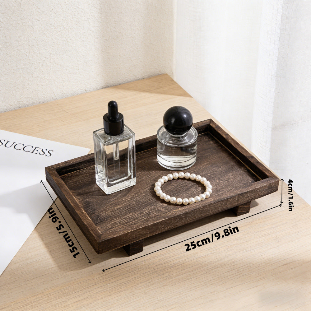 Hand placing a perfume bottle on a dark wood desk tray with a candle beside a table lamp – Pausadesk
