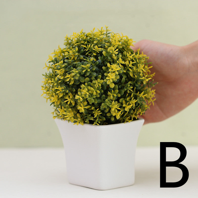 Yellow artificial mini plant in white square pot, held by hand for scale – Pausadesk