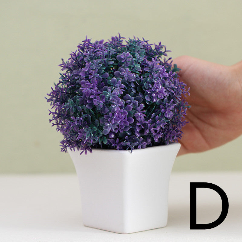 Purple artificial mini plant in white square pot, held by hand for scale – Pausadesk